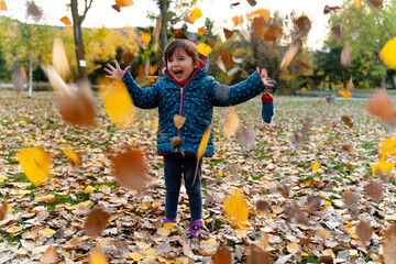 Little girl playing with autumn leaves outdoors