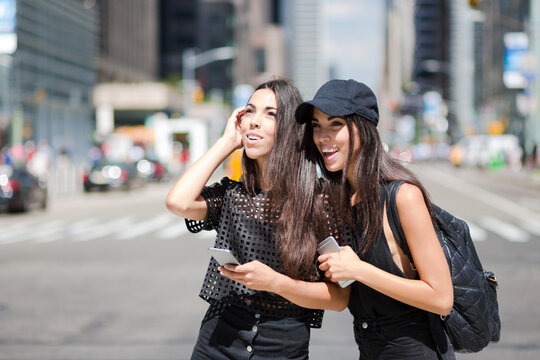 USA, New York City, two happy twin sisters with cell phones in Manhattan