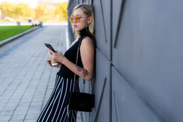 Fashionable young woman leaning against wall looking at smartphone