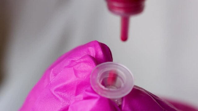 master permanent makeup attaching micro needle on tattoo machine or putting brown and red pigment in mini cup.woman in black or pink gloves, dark background.pen for micropigmentation.