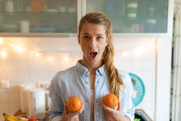 Portrait of young woman holding oranges at home