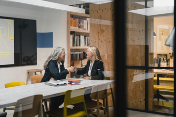 Happy mature and young businesswoman shaking hands in loft office