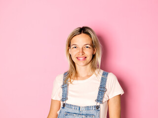 Portrait of smiling blond woman wearing dungarees in front of pink background