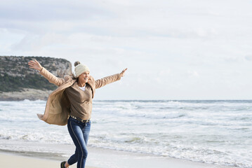 Spain, Menorca, happy senior woman running on the beach in winter