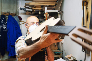 Craftsman with face mask examining guitar while standing at workshop