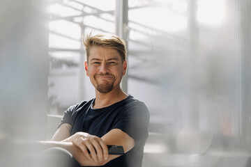 Portrait of a confident bearded man holding smartphone at the window