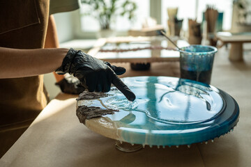 Resin art. Female artist applying epoxy resin with gloved fingers in art studio workshop. Closeup...