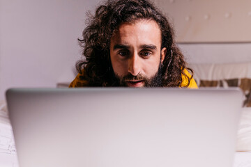 Young man in bed at home using laptop
