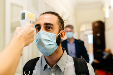Hand of female with infrared thermometer checking businessman's temperature in corridor