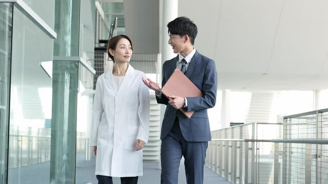 室内を歩く白衣を着た女性とスーツを着たビジネスマン