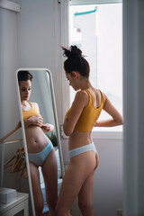 Young woman in underwear at home looking in mirror