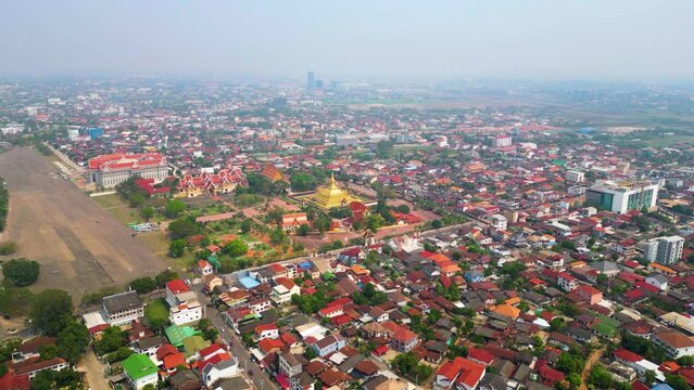 Aerial perspective of Pha That Luang, a Buddhist temple located in Vientiane, Laos, enveloped by the surrounding local residential area, portraying the integration of spirituality and everyday life.