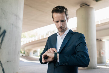 Businessman standing at underpass using smartwatch