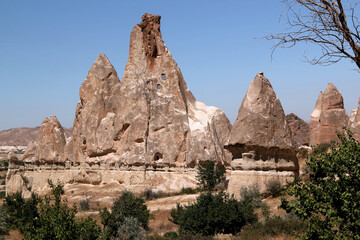 Fototapeta premium Landscape with cone-shaped mountains (also called Fairy Chimneys) with caves inside in the Rose Valley between the towns of Goreme and Cavusin in Cappadocia, Turkey