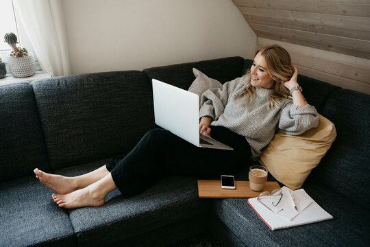 Smiling woman using laptop on sofa while freelancing at home