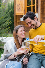 Happy man pouring wine in glass held by girlfriend while sitting outdoors