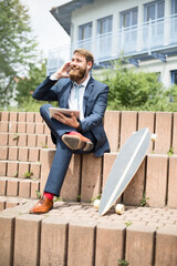 Businessman with skateboard, tablet and earphones on the phone