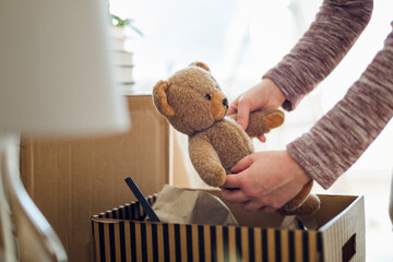 Close-up of woman unpacking cardboard box in new home taking out teddy bear