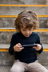 Boy sitting on stairs playing with handheld game console © tunedin
