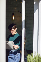 Woman standing at the window at home reading newspaper