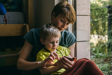 Mother and little son cuddling at home looking at smartphone
