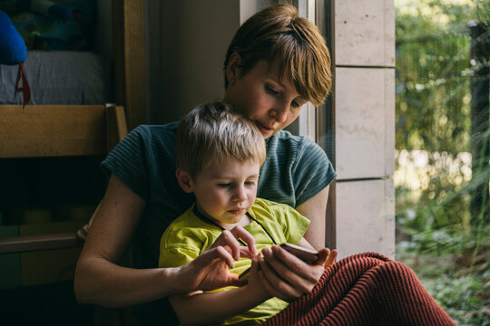Mother and little son cuddling at home looking at smartphone - Powered by Adobe