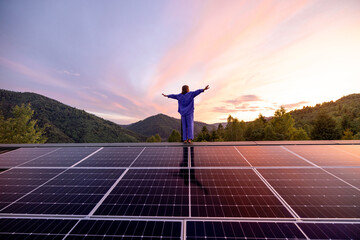 Rooftop with solar panels on house in mountains, woman stands alone enjoying sunset. Energy independence, sustainability, self sufficient, and escapism to nature concept
