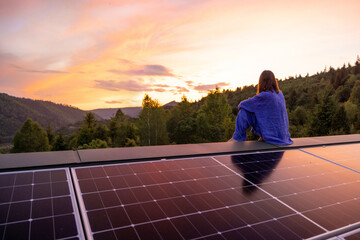 Rooftop with solar panels on house in mountains, woman sitting alone enjoying sunset. Energy...