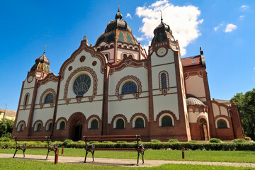 The entire facade around the side entrance of the Synagogue of Subotica on a sunny day, two little benches are standing in the foreground, Subotica, Serbia