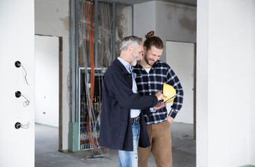 Architect and construction worker discussing over digital tablet while standing in renovating house