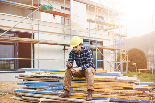 Worker on a construction site having a break checking cell phone