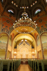 Obraz premium Inside the Synagogue of Subotica, a big golden chandelier is hanging from the colorful ceiling over the the benches and the aisle leading to the altar, Subotica, Serbia