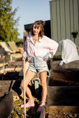 Portrait of a young woman works on her backyard garden, mulching with rack paths between the beds....