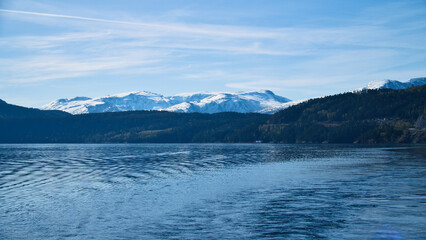 Norwegian fjord landscape. Blue water overlooking mountains with snow-covered peaks