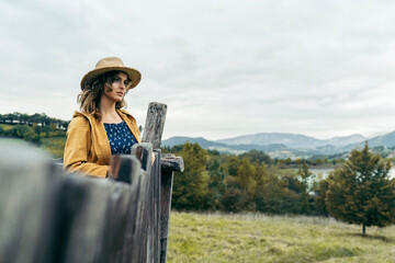Young curly haired woman wearing a hat, yellow coat and blue t-shirt looking the mountain landscape