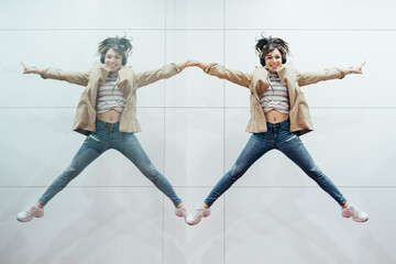 Happy woman with headphones jumping in the air reflected in mirror