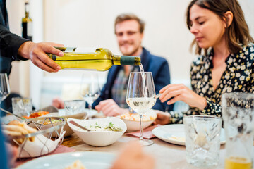 Friends dining in an Indian restaurant, waiter pouring wine in glasses