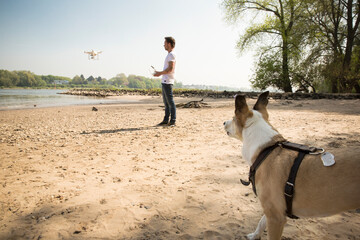 Man with a dog flying drone at a river