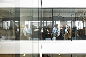 Businesswoman and empoyees talking behind windowpane in office