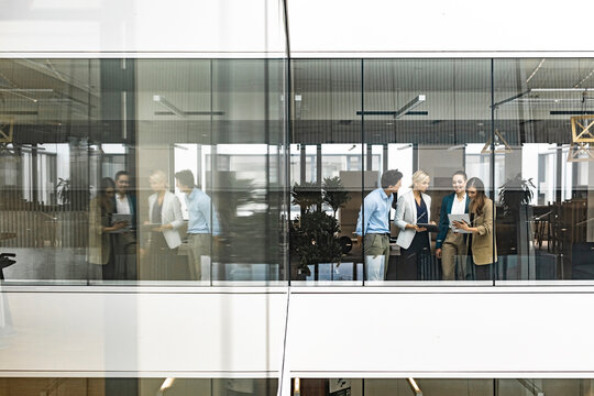 Businesswoman and empoyees talking behind windowpane in office
