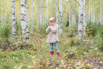 Blond girl playing Hide and Seek in a birch forest