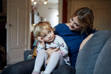 Mother and little daughter sitting together on the couch at home