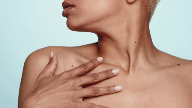 A tasteful close-up of the neck and collarbone area of a woman against a calm blue background. Unrecognizable seductive female touching clean skin