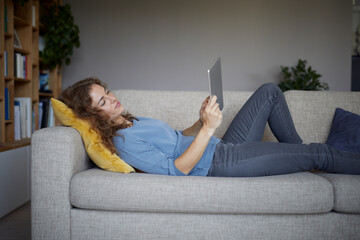 Woman using digital tablet while lying on sofa at home