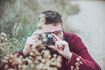 Bearded man taking photo of flowers with vintage camera