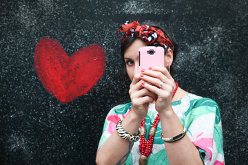 Woman taking a selfie next to heart painted on the wall