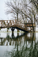 Beautiful original retro wooden bridge over a small river, wooden house behind. The reflection of the bridge in the pond. Small town Bijeljina in Bosnia and Herzegovina. Stanisici Ethno Village