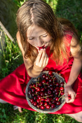 Girl sitting on a meadow eating cherries