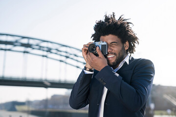 Smiling man in suit at the riverside taking a picture with a vintage camera