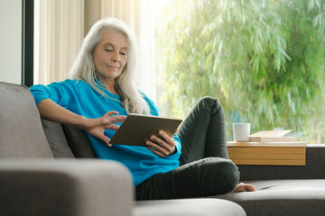 Portrait of mature woman sitting on the couch at home using digital tablet